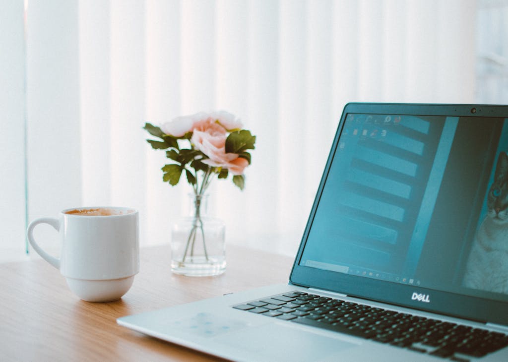 Comfortable home office desk with laptop, coffee mug, and flower vase.